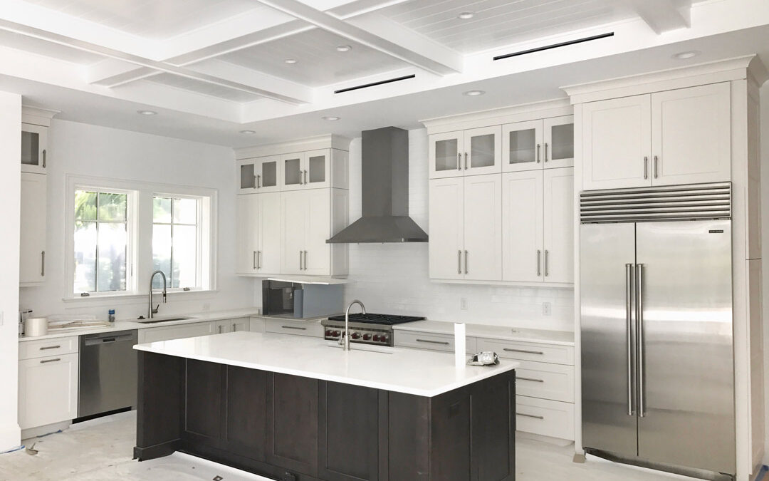 Modern white kitchen with coffered ceilings, dark island, and stainless steel appliances.